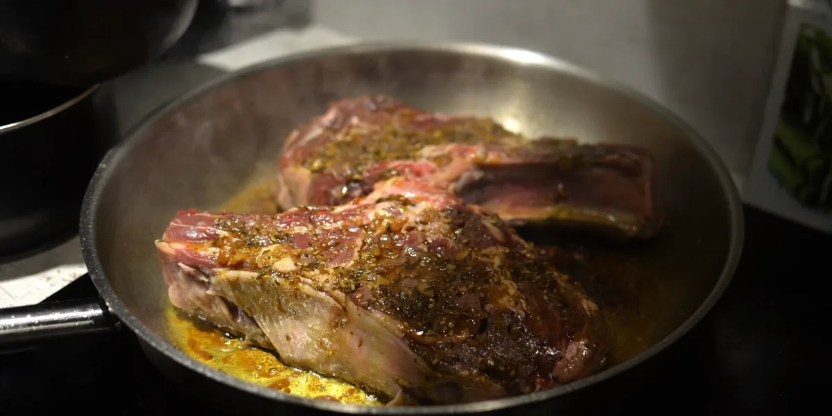 Two seasoned steaks searing in a stainless-steel frying pan on a home stovetop